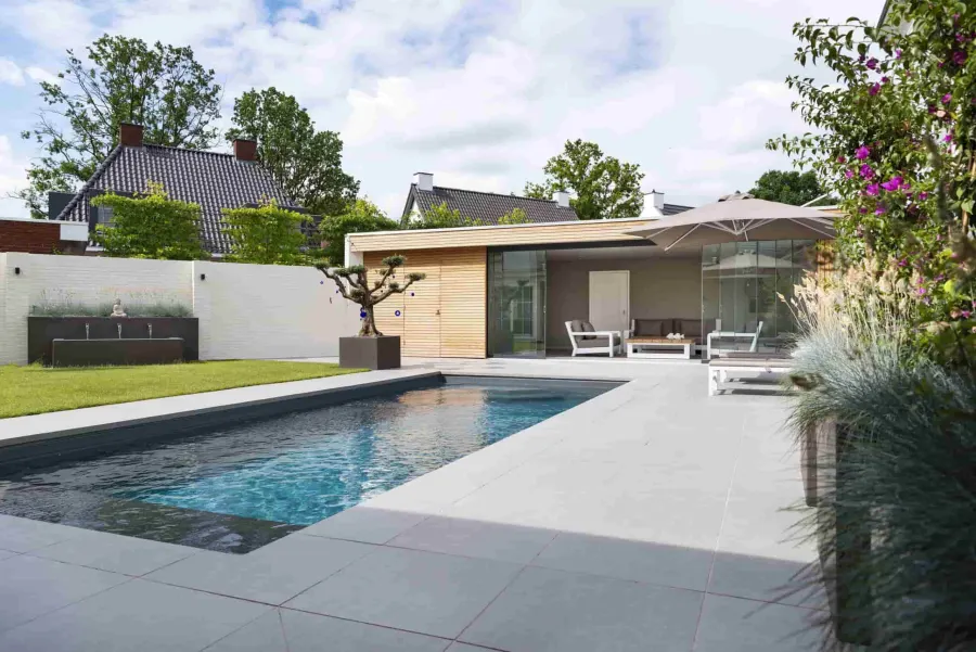 Composiet zwembad met antracietkleurige kuip in een strak aangelegde tuin met poolhouse en terras
